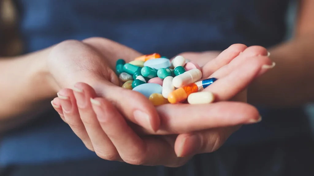 A person holds a handful of various colorful pills and capsules.